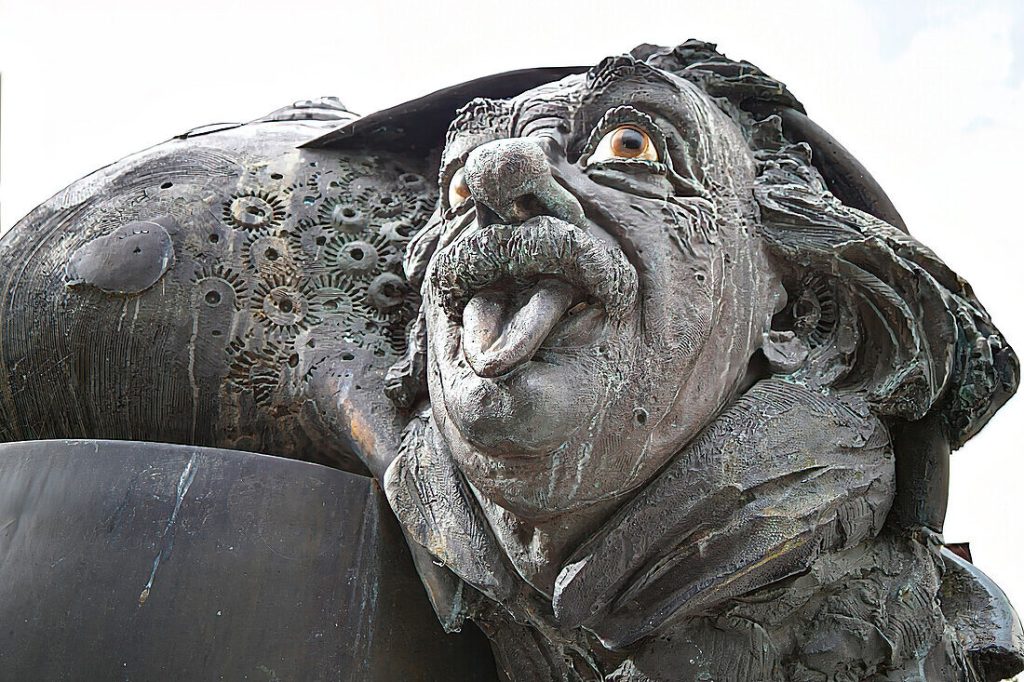Close-up outdoor view of a bronze scientist statue with a playful expression