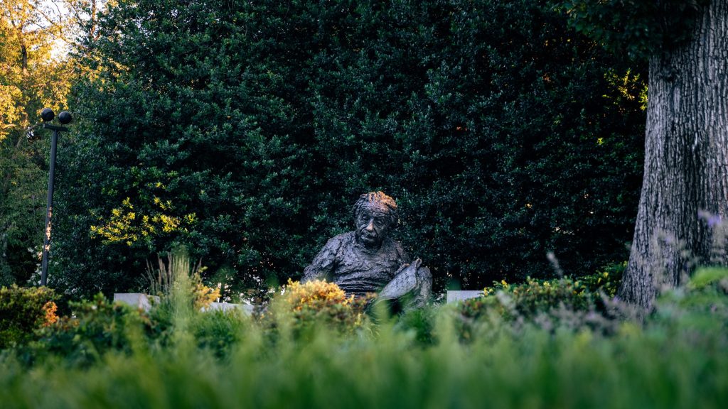 Outdoor bronze scientist statue surrounded by garden greenery