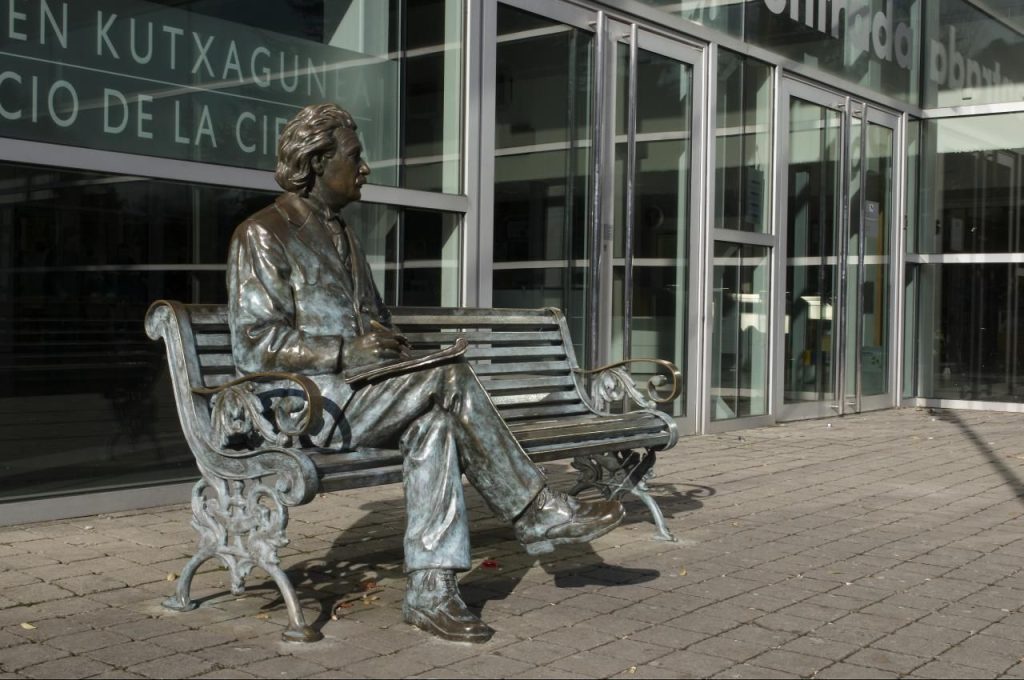Bronze scientist statue sitting on a bench outside a building