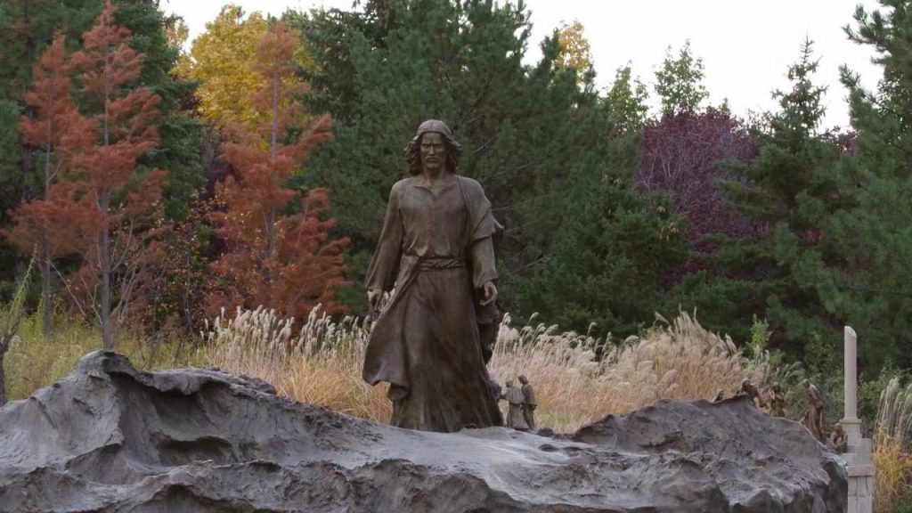 A statue of Jesus walking on rocky ground in a forest setting